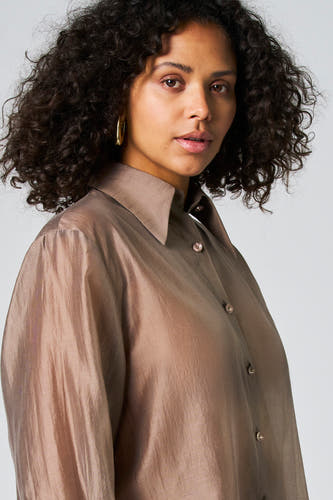 Blouse taupe à longues manches d'Astrid Black Label, avec des boutons roses clairs et une texture brillante.