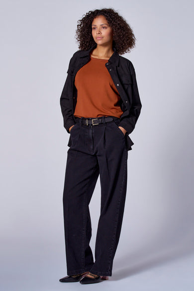 Manteau noir en imitation de Astrid Black Label, porté sur une chemise brune et un pantalon noir.