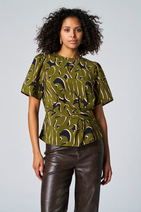 Groene blouse met driekwart mouwen van Astrid Black Label, met een abstract patroon en gedrapeerde taille, gecombineerd met een leren broek.
