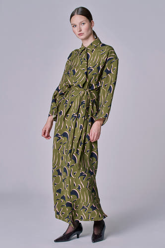 Groene jurk met lange mouwen van Astrid Black Label, met patroon van donkerblauwe en roze vormen, gedragen met zwarte pumps.
