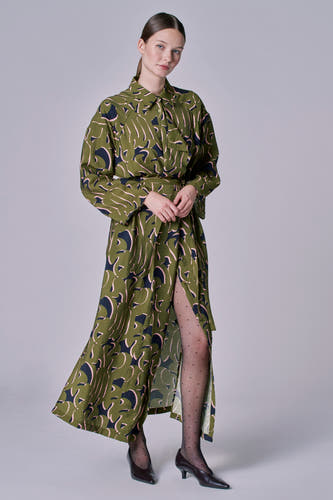 Robe verte à longues manches d'Astrid Black Label, avec un motif de feuille abstrait, fendue à l'avant et sous-pantalon noir.