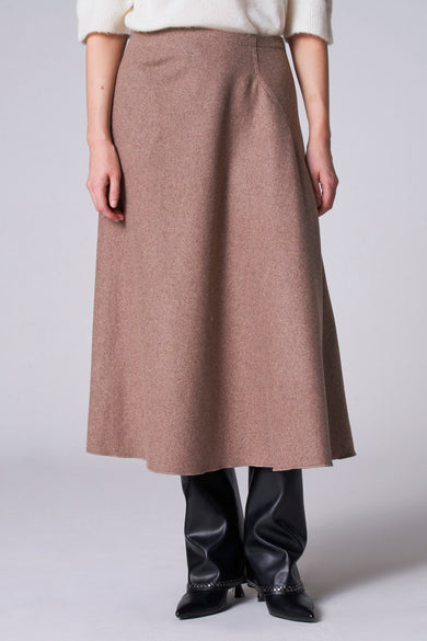 Lange taupe rok van Astrid Black Label, vallend over een zwarte leren broek en puntige schoenen.
