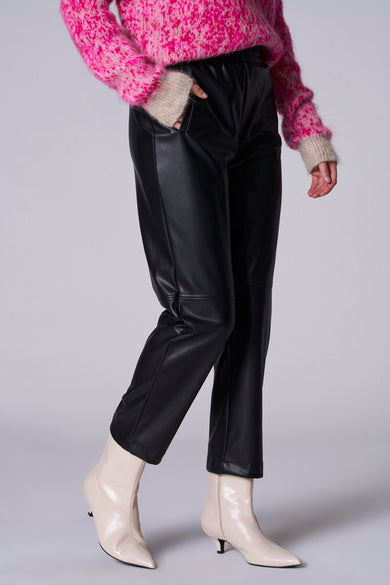 Pantalon noir d'Astrid Black Label, avec un look en cuir et associé à des bottes crème et une chemise rose.