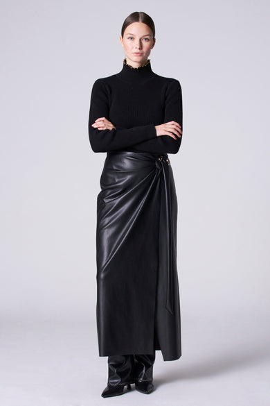 Robe noire Astrid Black Label avec drapé et accents dorés, associée à une veste noire et des bottes en cuir.