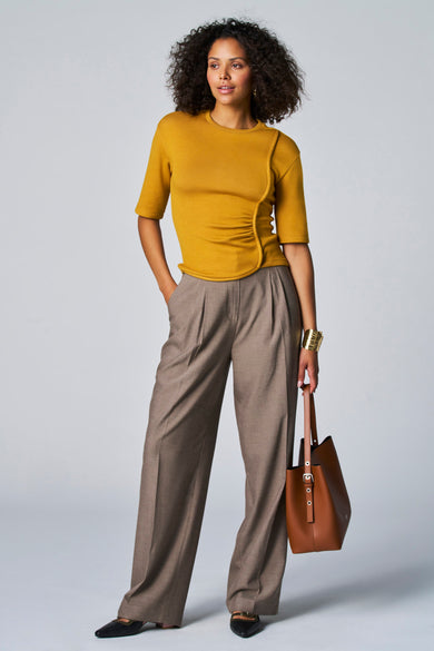 T-shirt jaune à manches courtes d'Astrid Black Label, avec un détail asymétrique raffiné et associé à un pantalon marron et une sacoche en cuir.
