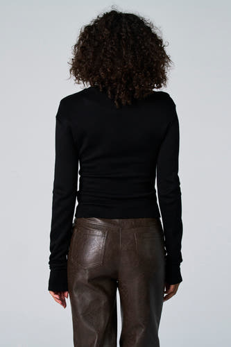 T-shirt noir à manches longues d'Astrid Black Label, avec des cheveux bouclés et un pantalon en cuir brun.