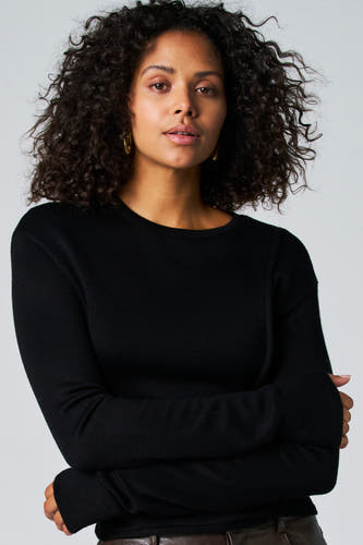 T-shirt noir à manches longues d'Astrid Black Label, avec des bras croisés et des boucles d'oreilles dorées.