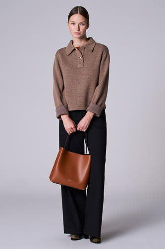 Veste taupe avec col en V d'Astrid Black Label, à longues manches et portée avec un pantalon noir et une poche main marron.