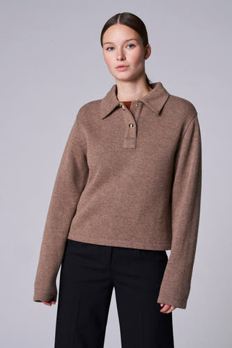 Veste taupe avec col en V d'Astrid Black Label, à longues manches, portée avec un pantalon noir.
