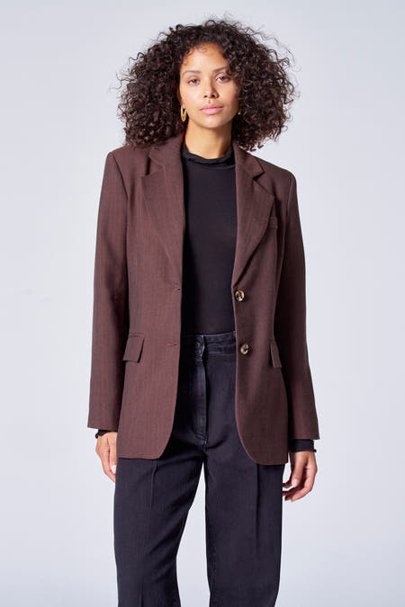 Blazer marron d'Astrid Black Label, porté avec un pull-over noir et des jeans foncés, avec des boucles d'oreilles dorées.