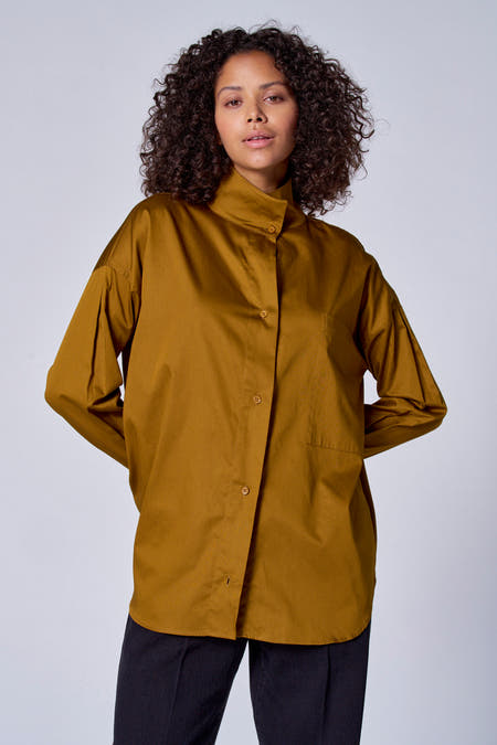 Blouse verte avec manches longues d'Astrid Black Label, à boutons et avec une poche poitrine, portéeéeée un pantalon.