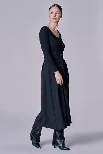 Robe noire à longues manches d'Astrid Black Label, avec une ceinture à la taille et des bottes en cuir.
