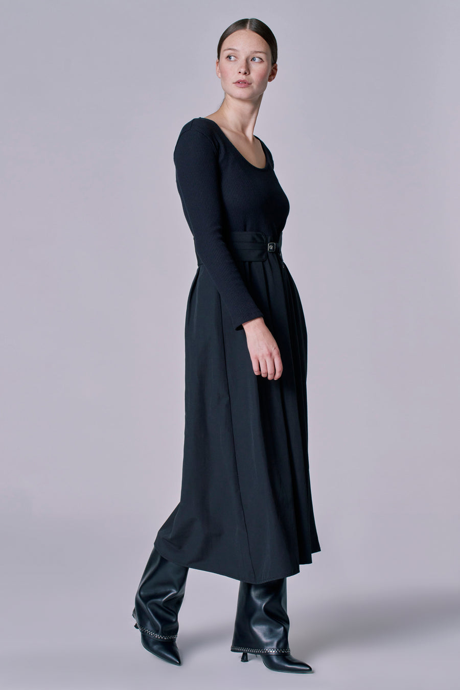 Robe noire à longues manches d'Astrid Black Label, avec une ceinture à la taille et des bottes en cuir.