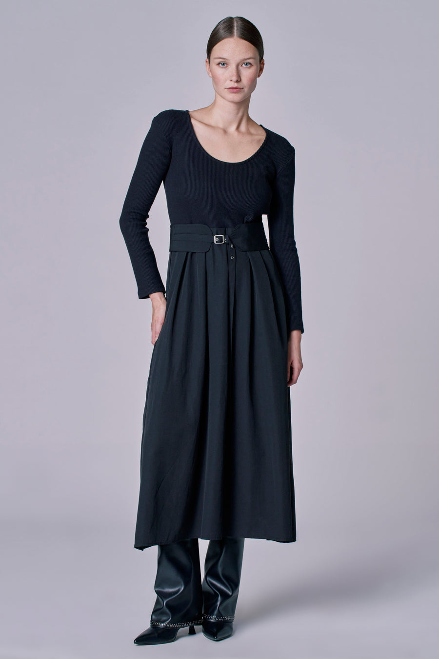 Robe noire à longues manches d'Astrid Black Label, associée à une ceinture de taille et des bottes en cuir avec détails.
