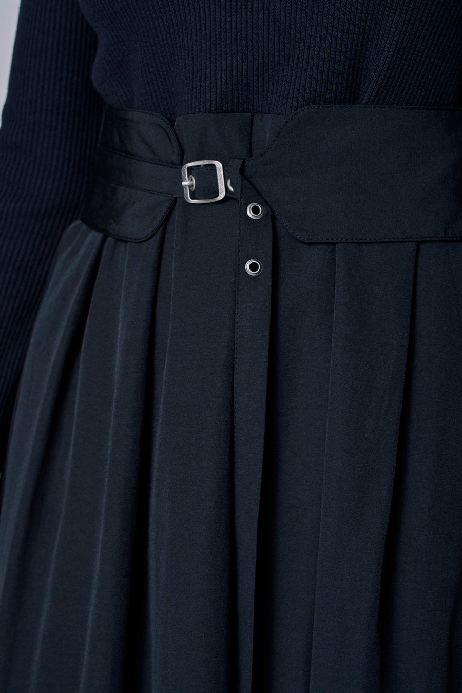 Robe noire à longues manches d'Astrid Black Label, avec des plis et une ceinture avec une boucle argentée.