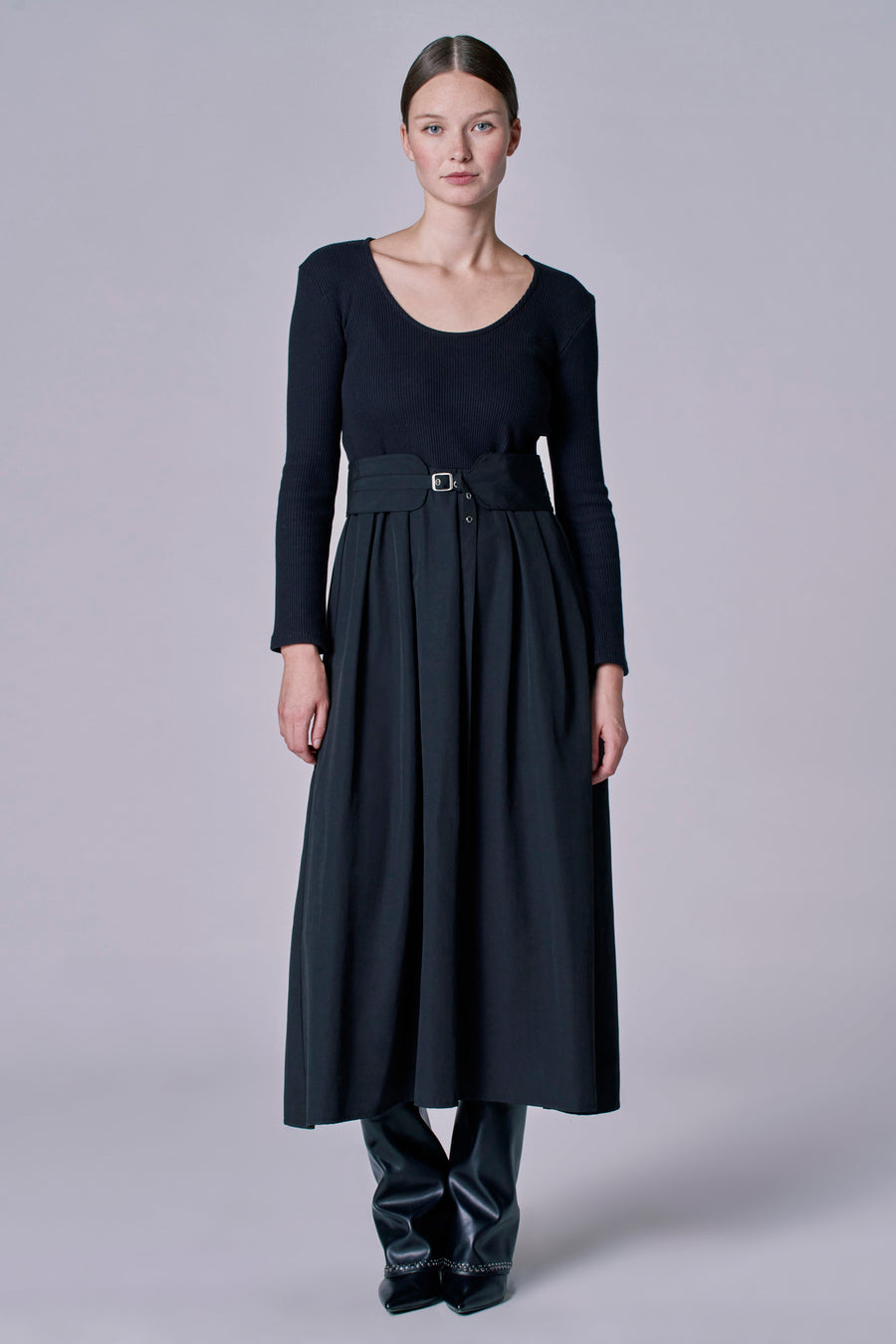 Robe noire à longues manches d'Astrid Black Label, avec une ceinture à la taille et des bottes en cuir.