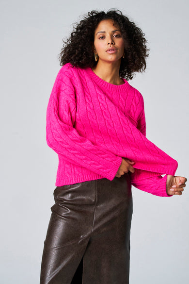Pull-over rond en rose Astrid Black Label, porté avec un jupe cuir marron, à longues manches.