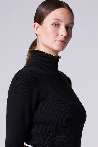 Gilet noir à col montant d'Astrid Black Label, avec une texture côtelée et des détails décoratifs dorés sur le col.