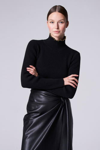Collier noir Astrid Black Label, avec des strass dorés le long du col et une texture à larges bretelles, associé à une jupe en cuir noir.
