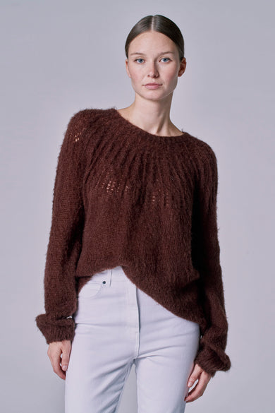 Bruine trui met ronde hals van Astrid Black Label, met een losse, pluizige textuur en witte jeans.
