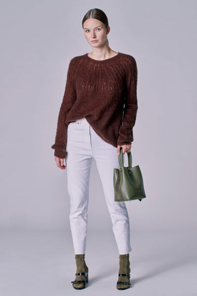 Pull marron avec col rond d'Astrid Black Label, à la coupe décontractée, porté avec des jeans blancs et une poche verte.