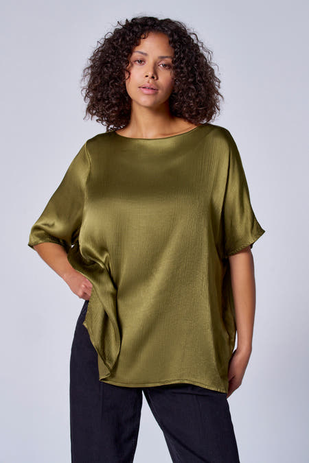 Blouse verte avec manches courtes d'Astrid Black Label, à texture brillante et portée avec un pantalon noir.