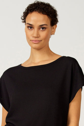 Vrouw draagt zwarte blouse, witte achtergrond.
