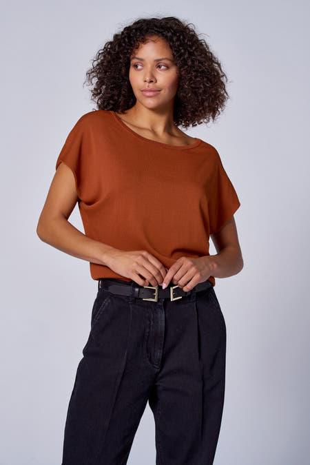 Maillot orange avec col rond d'Astrid Black Label, vu de dos, associé à des jeans noirs.