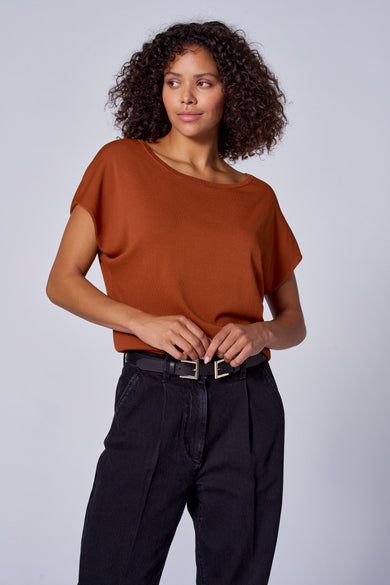 Maillot orange avec col rond d'Astrid Black Label, vu de dos, associé à des jeans noirs.