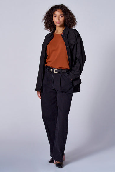 Chemise orange à col rond d'Astrid Black Label, associée à un pantalon noir avec ceinture et une veste.