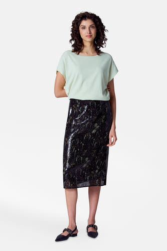 T-shirt vert avec col rond d'Astrid Black Label, porté avec une jupe noire brillante et des chaussures noires.