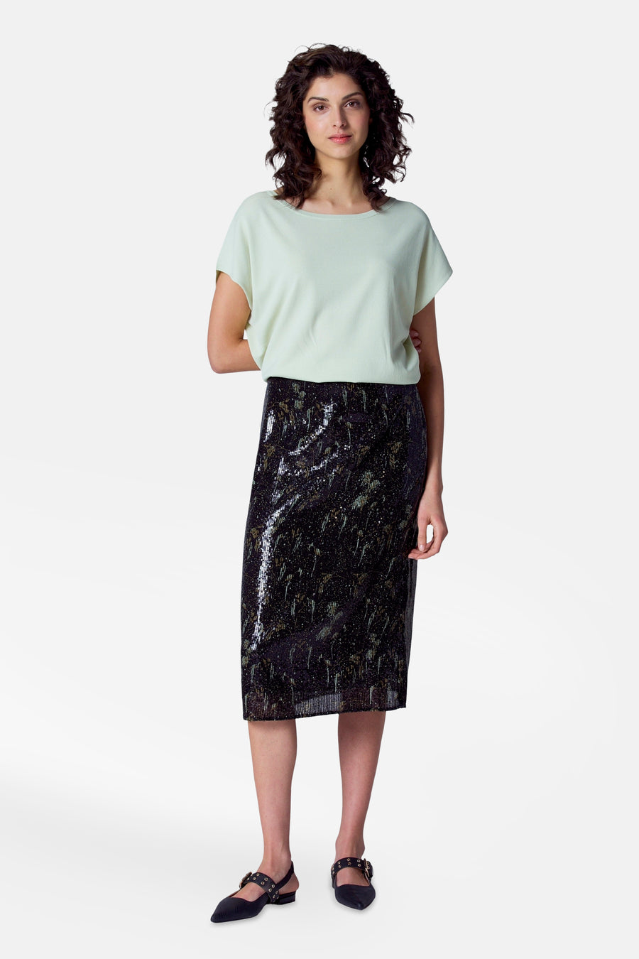 T-shirt vert avec col rond d'Astrid Black Label, porté avec une jupe noire brillante et des chaussures noires.