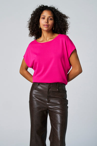 T-shirt rose avec col rond d'Astrid Black Label, porté avec un pantalon de cuir marron et des boucles d'oreilles dorées.