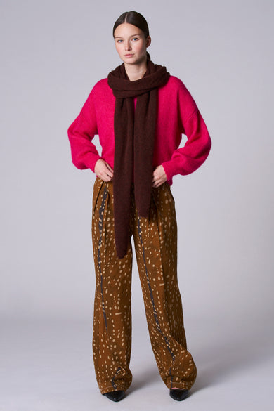 Gilet rose d'Astrid Black Label, avec une texture moelleuse, porté sur un haut marron et un pantalon imprimé.