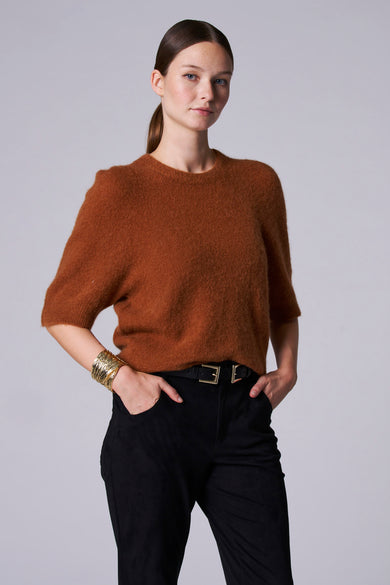 Pull marron avec col rond d'Astrid Black Label, vu de derrière, associé à un pantalon noir et un bracelet en or.