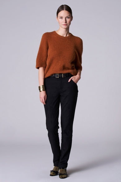 Pull marron avec col rond d'Astrid Black Label, associé à un pantalon noir, une ceinture et un bracelet en or.