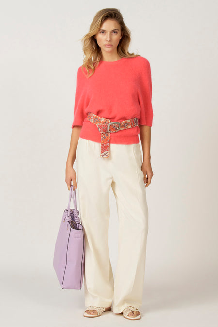 Vrouw, rode trui, ecru broek, paarse tas, riem.
