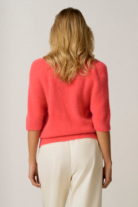 Vrouw draagt roze trui en crèmekleurige broek.