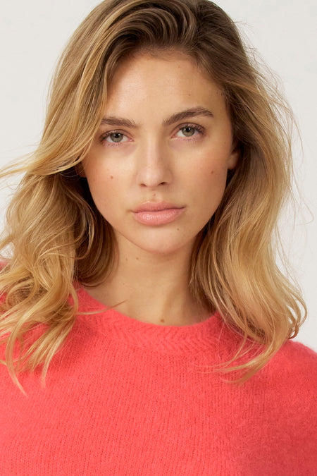 Portret van een blonde vrouw met een koraalkleurige trui.
