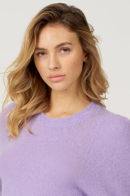 Jonge vrouw met blond haar in paarse trui.
