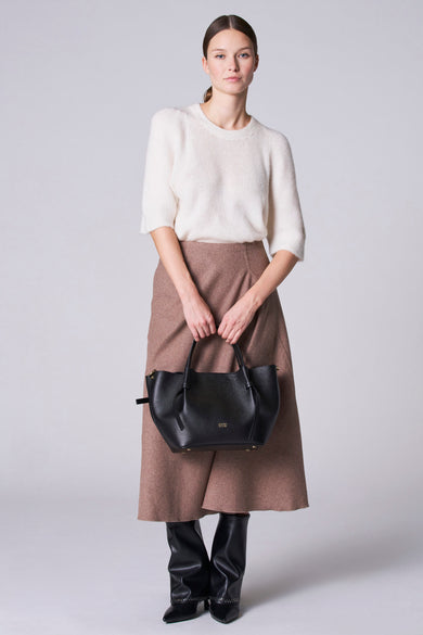 Pull-over blanc avec col rond d'Astrid Black Label, porté avec une jupe marron et des bottes noires.