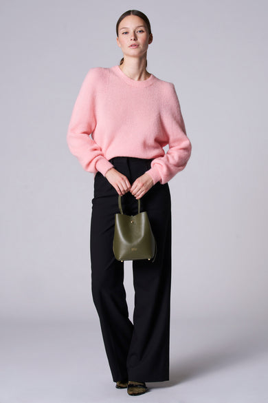 T-shirt rose avec col rond d'Astrid Black Label, porté avec un pantalon noir et une poche verte.