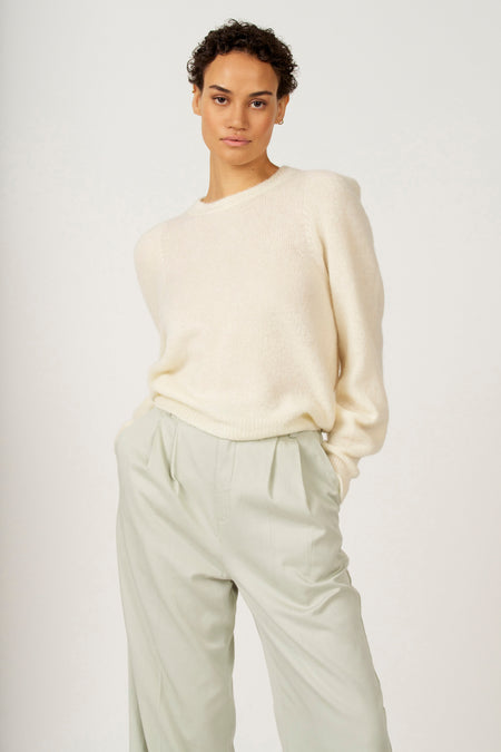 Vrouw in een beige trui en lichtgroene broek.