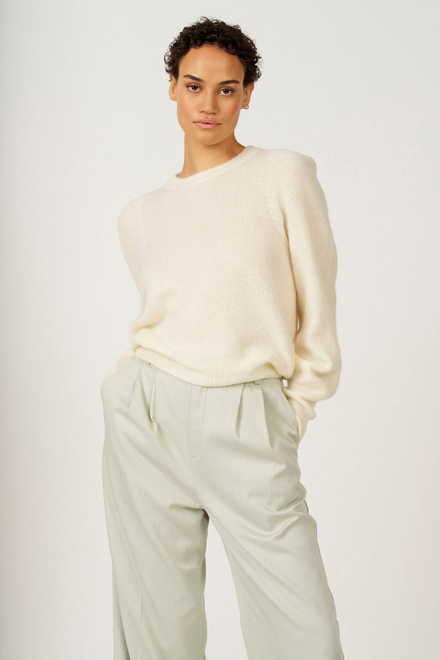 Vrouw in een beige trui en lichtgroene broek.