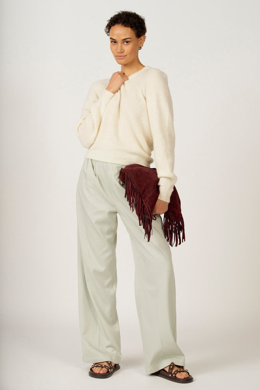 Tunique écru avec col rond d'Astrid Black Label, portée avec un pantalon vert clair large et des sandales brunes.