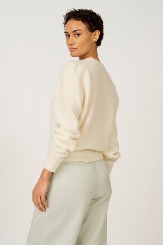 Vrouw in crèmekleurige trui en mintgroene broek, staand.