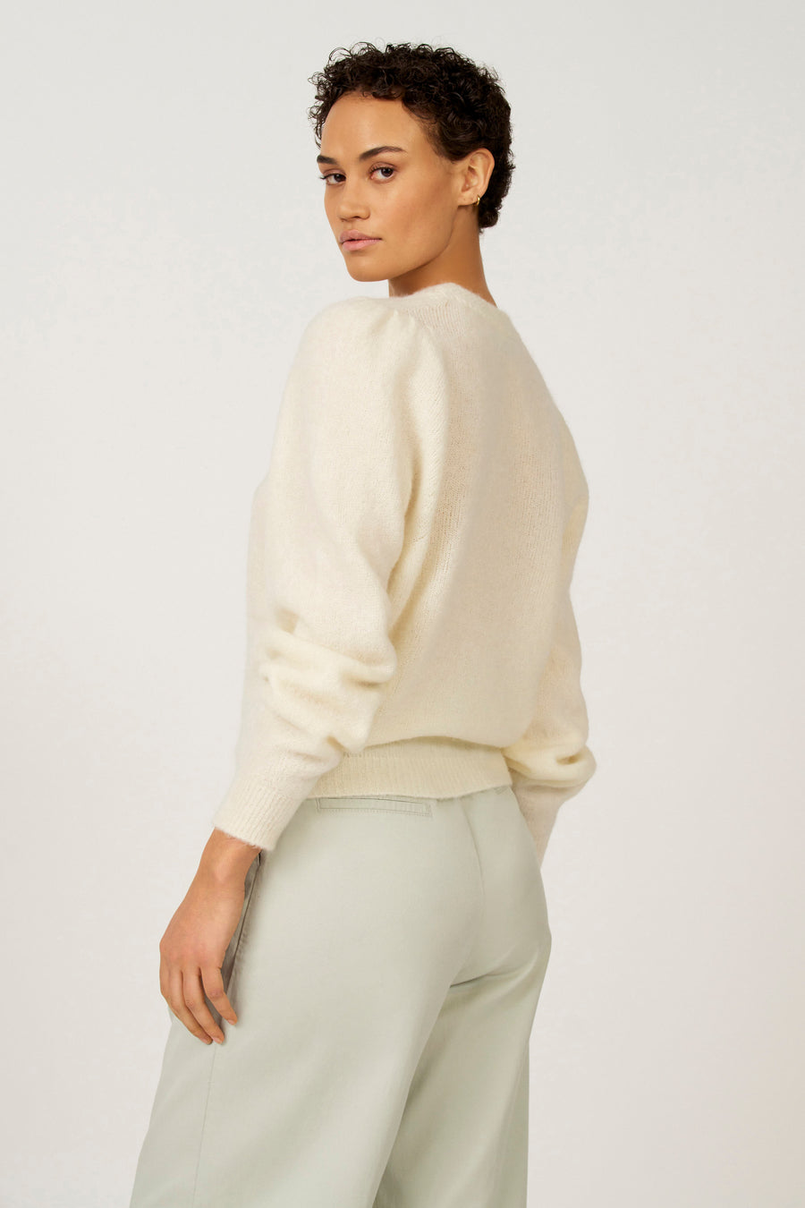 Vrouw in crèmekleurige trui en mintgroene broek, staand.