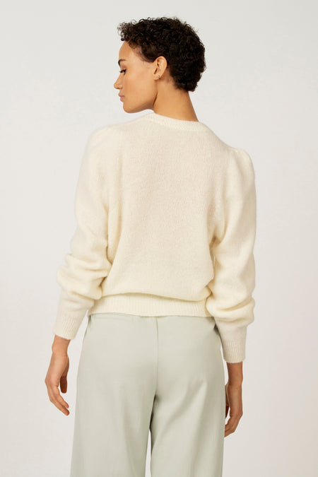 Achterkant van een vrouw in een gebroken witte trui en lichtgroene broek.