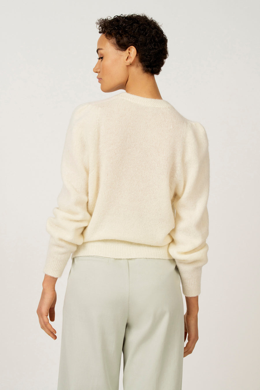 Achterkant van een vrouw in een gebroken witte trui en lichtgroene broek.