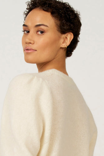 Vrouw met een witte, zachte trui die over haar schouder kijkt.